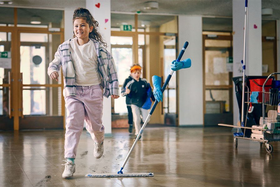 Lapset juoksevat kuraisin kengin koulun käytävällä, näkymätön siivooja puhdistaa lattiaa, ammattiliitto JHL puolustaa siivojia.